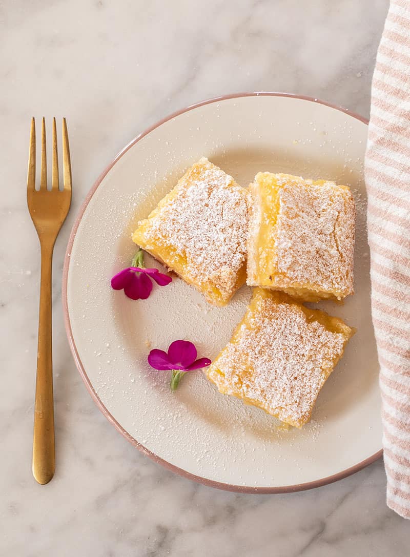 Lemon bars on a plate with a gold for and edible flowers.