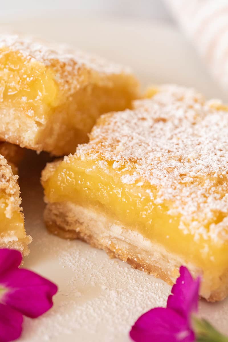 Easy homemade lemon bars with shortbread crust on a white plate with edible flowers in the foreground. 