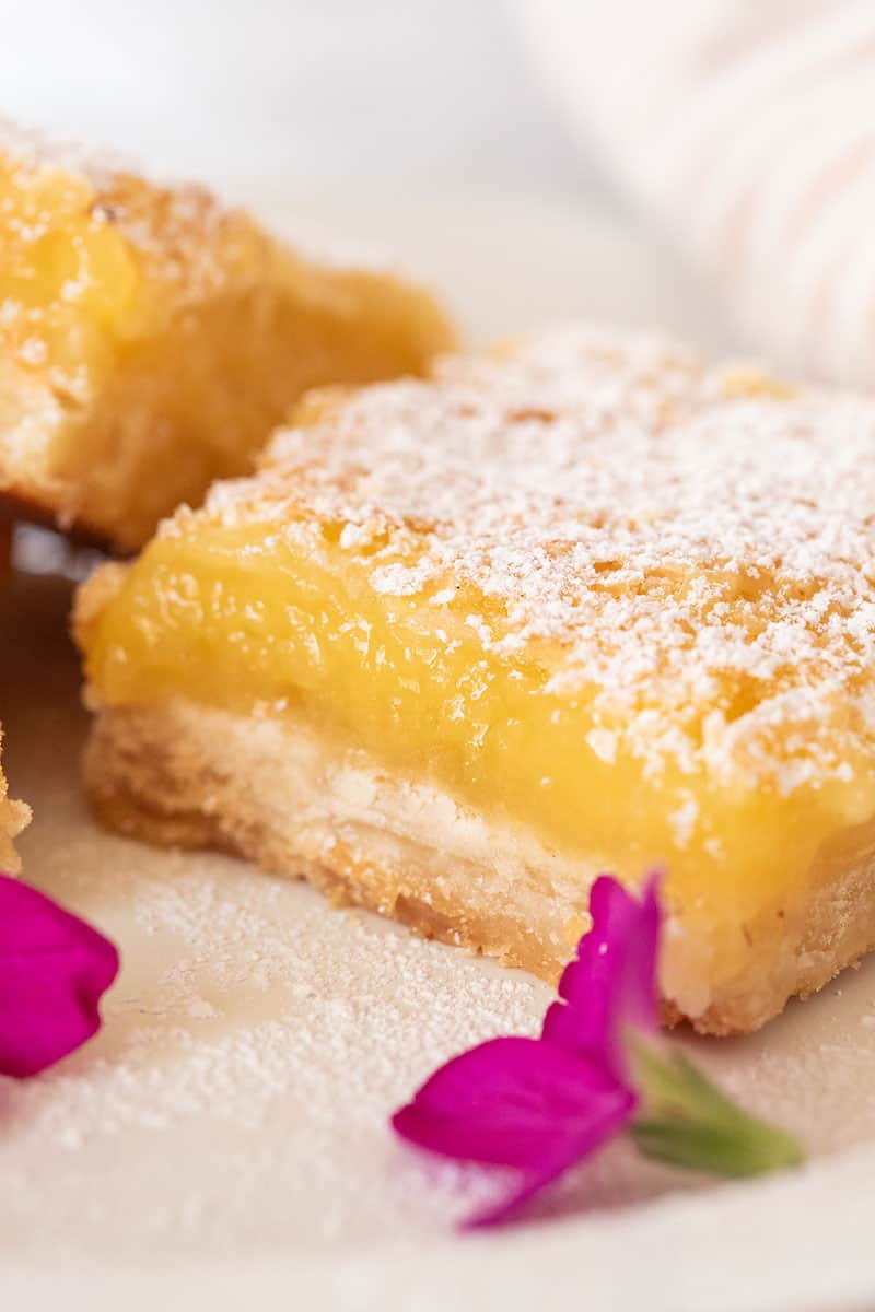 Close-up picture of a lemon bar with powdered sugar and edible pink flowers.