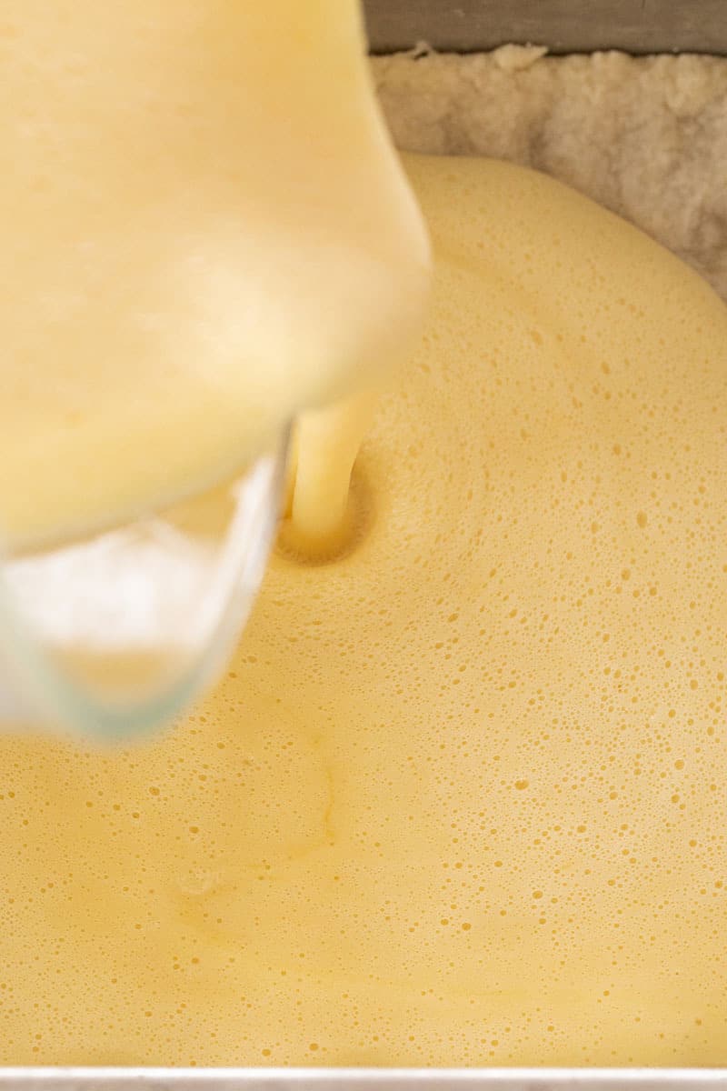 Pouring lemon batter into a crust to make lemon bars.