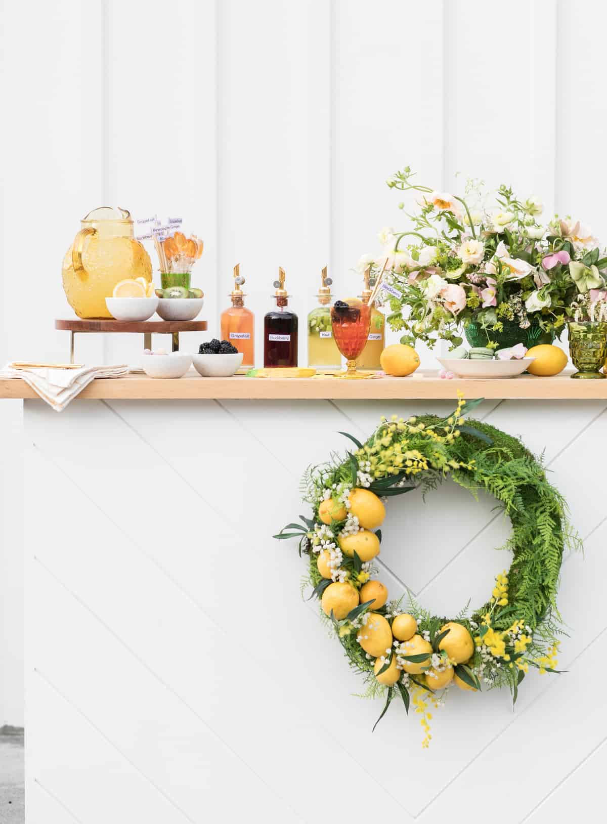 white lemonade stand with homemade syrups, lemon wreath, flowers. 