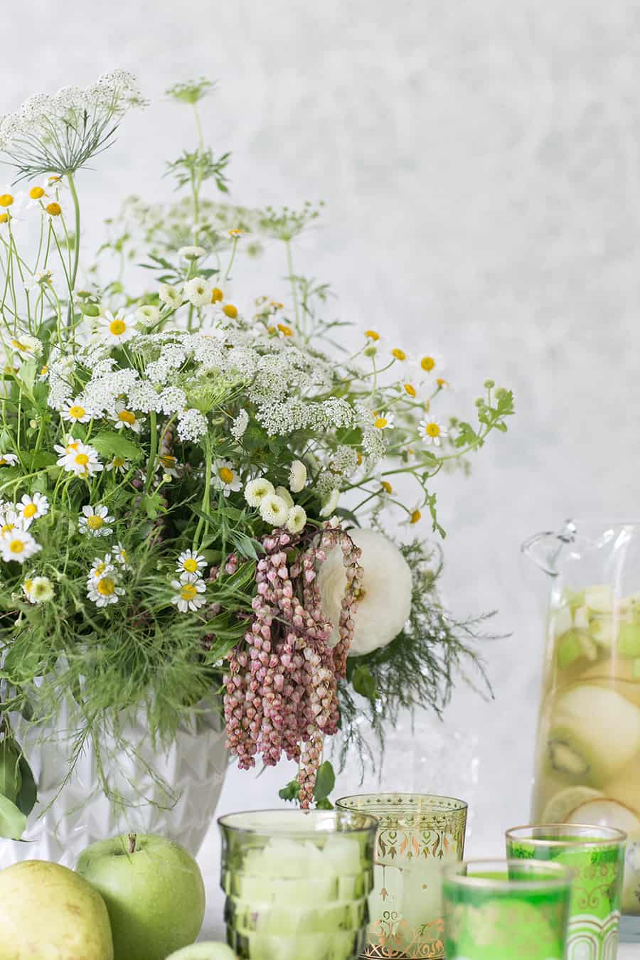 Flowers and green glasses filled with Green Irish Whiskey Sangria 