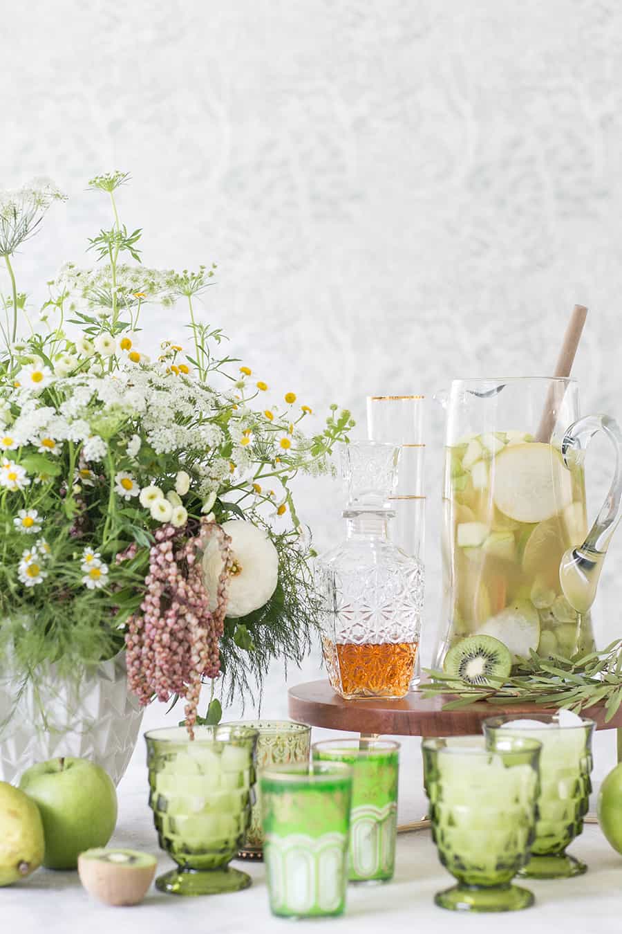 Green Irish Whiskey Sangria, green glasses and a decanter with beautiful flowers for St. Patrick's Day.