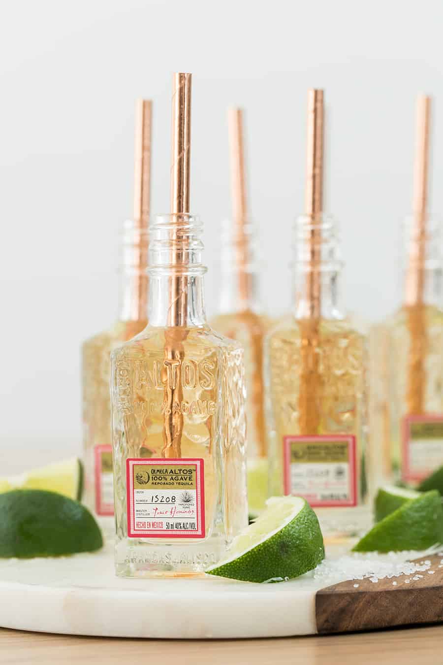 Tiny tequila shots in mini tequila bottles with a copper straw and a lime wedge.