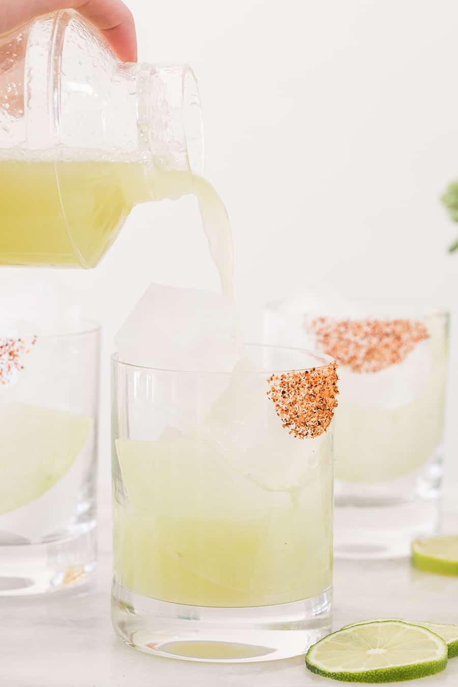 Pouring honeydew margarita into a glass from a clear cocktail shaker.