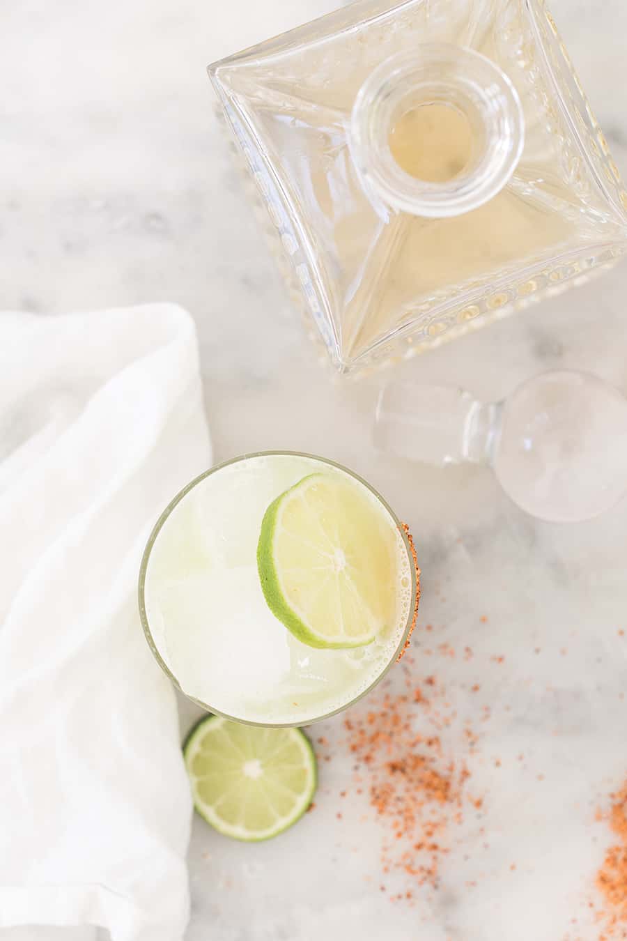 Cocktail with lime wedge and a bottle of tequila. 