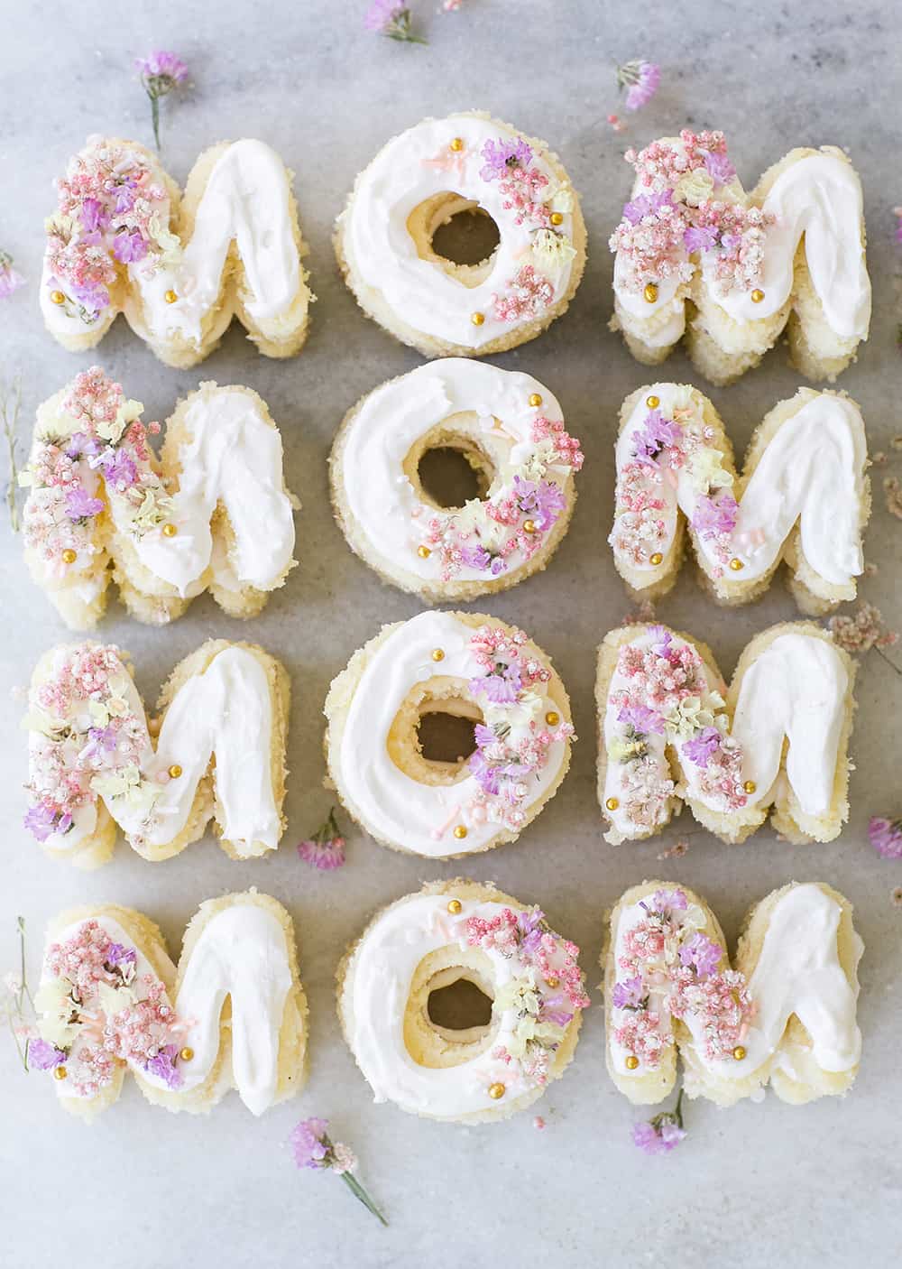 Mini Mother's Day Cakes that spell mom on a marble table with flowers and sprinkles.
