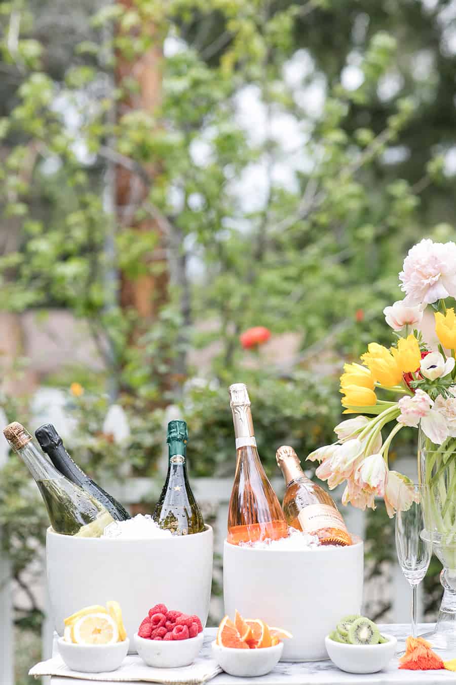 Bottles of Champagne over ice with bowls of fruit.