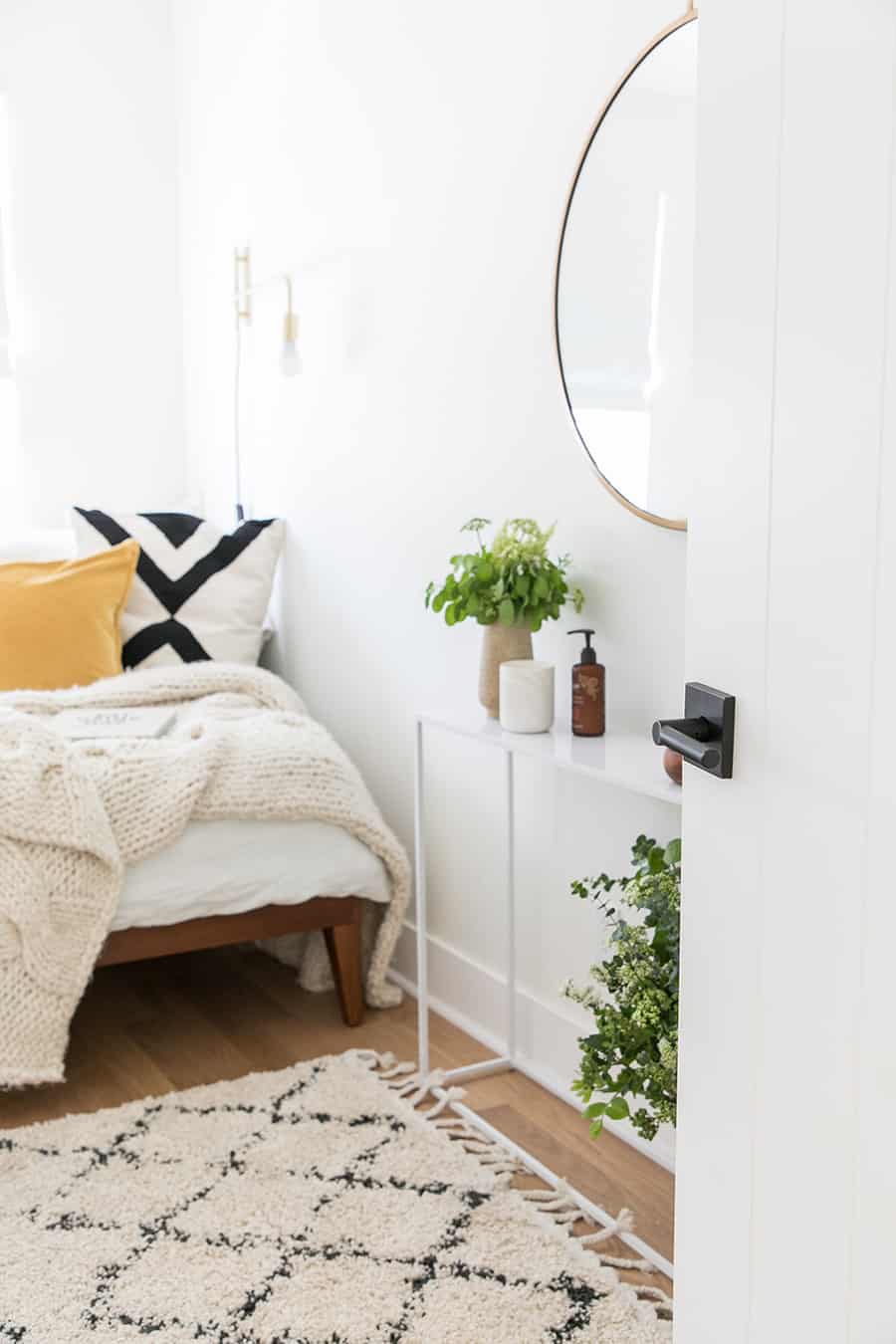 Door open to a guest bedroom with a bed, mirror and pillows.