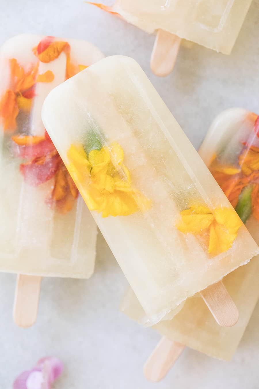 Three Ingredient Honey Lemonade Popsicles with edible flowers and lemons on a marble table.