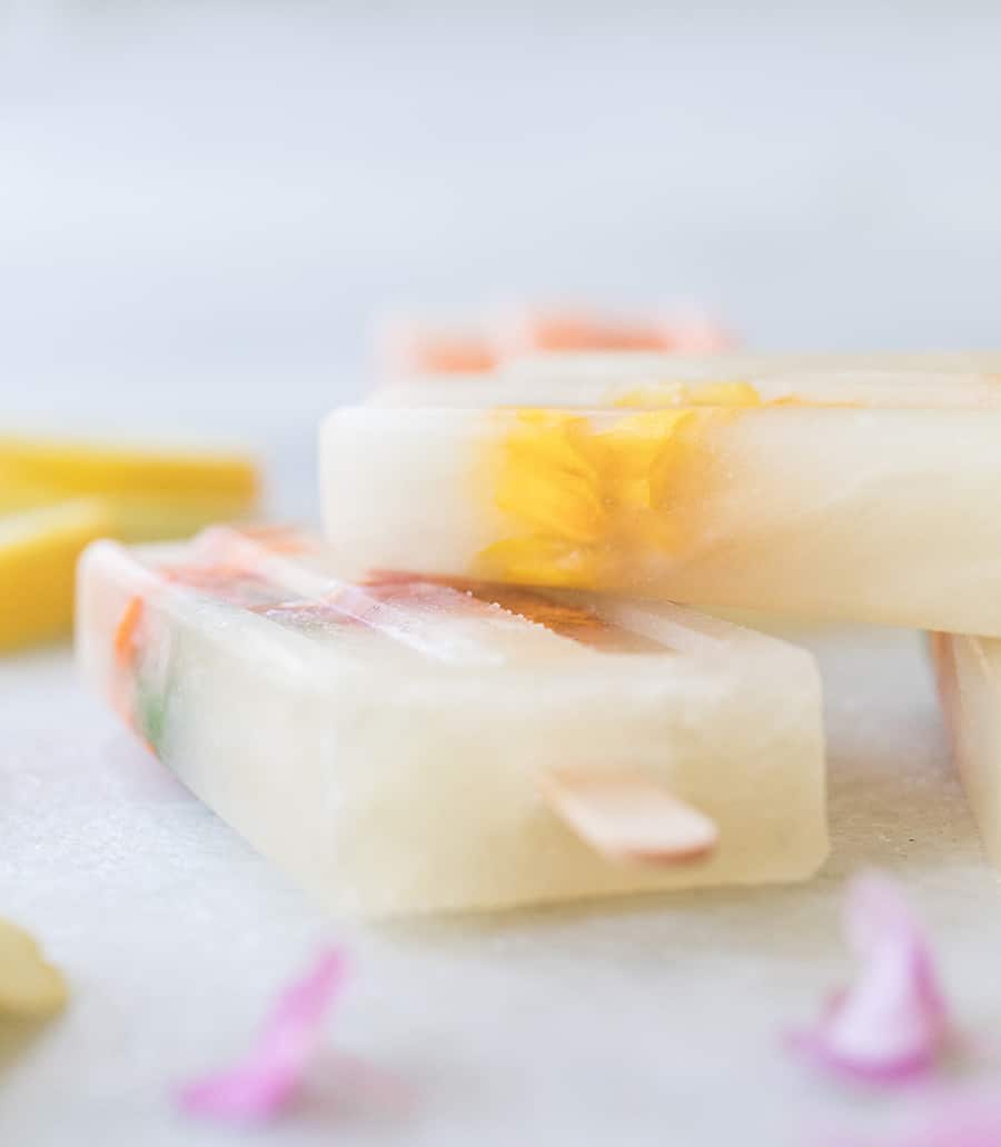 Three Ingredient Honey Lemonade Popsicles with edible flowers and lemons on a marble table.
