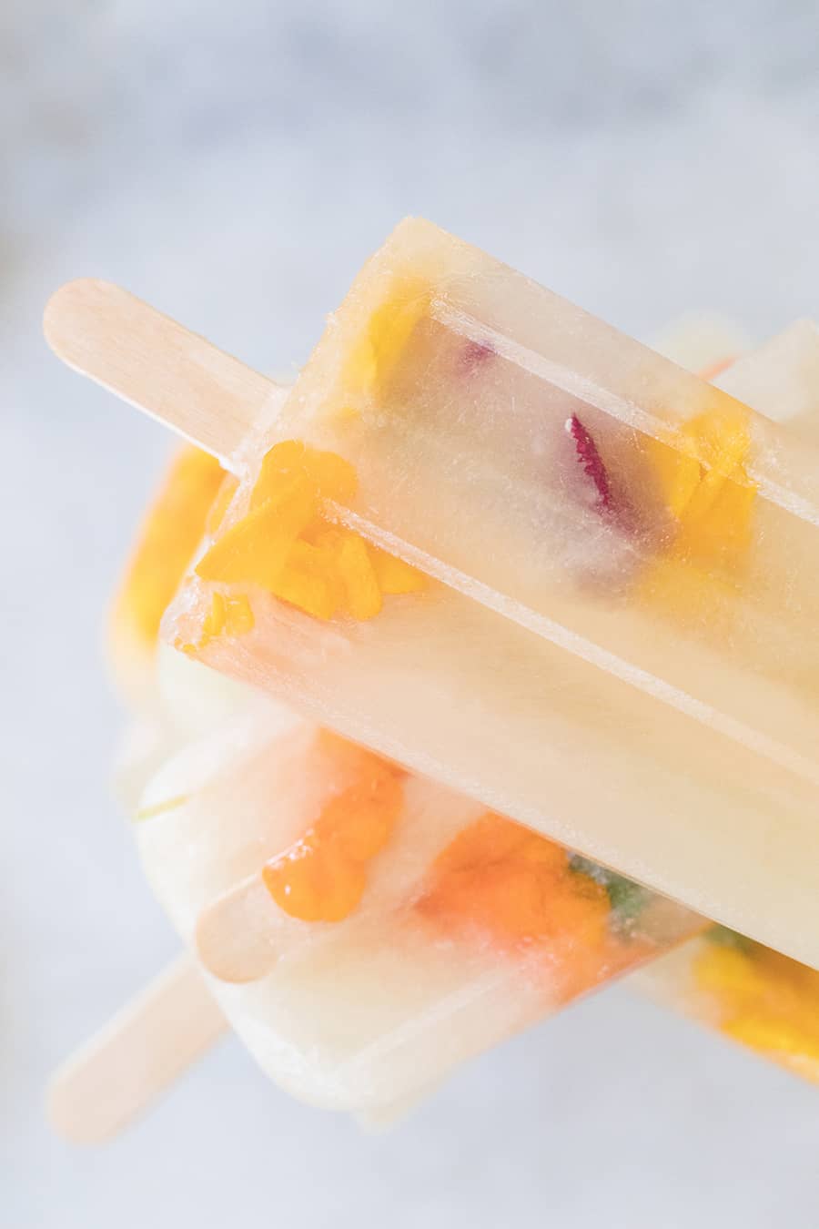 Three Ingredient Honey Lemonade Popsicles with edible flowers and lemons on a marble table.