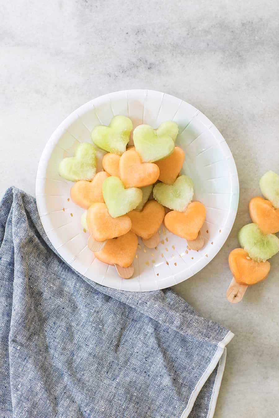 Heart fruit kabobs on a paper plate.