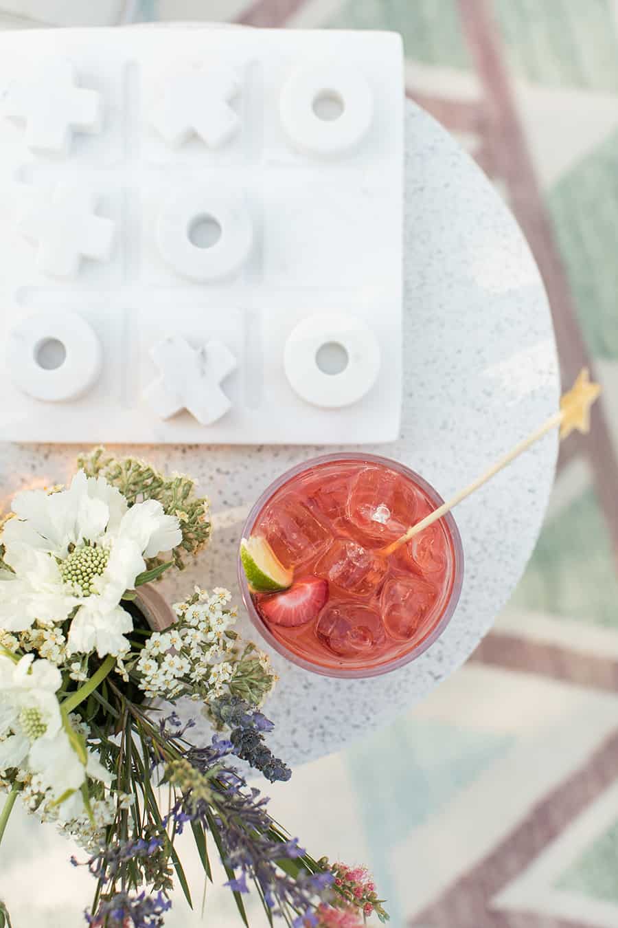 red cocktail on a table with flowers and a tic-tac-toe board. 