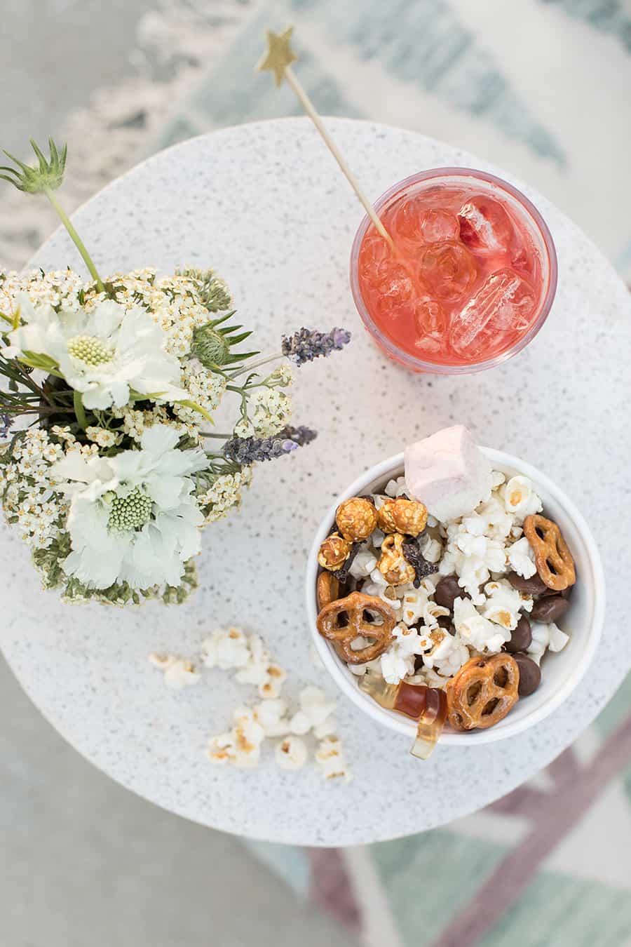 overhead photo of red cocktail and a bowl of popcorn with flowers on an outdoor table.