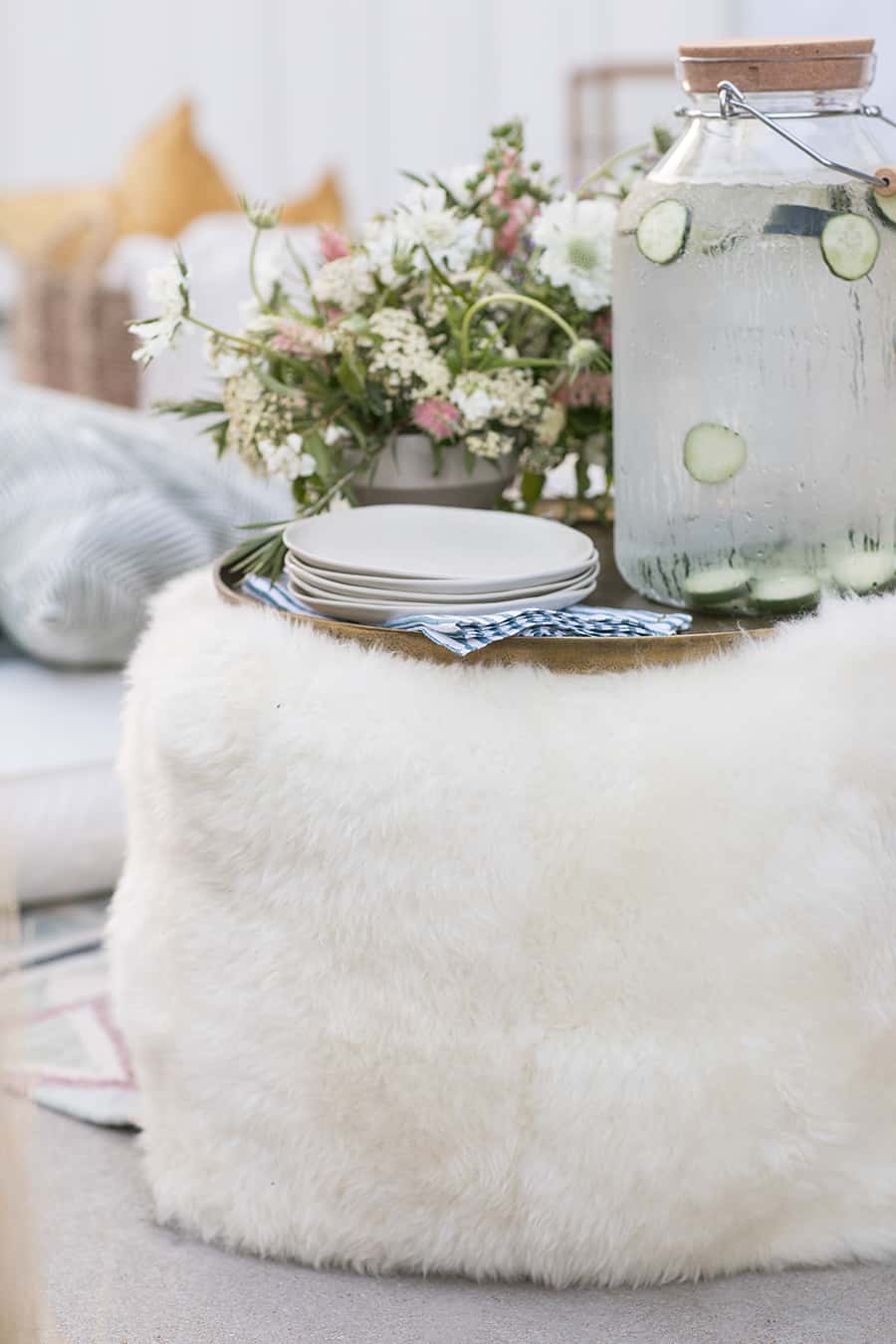 White pillow pouf with gold tray and plates and water.