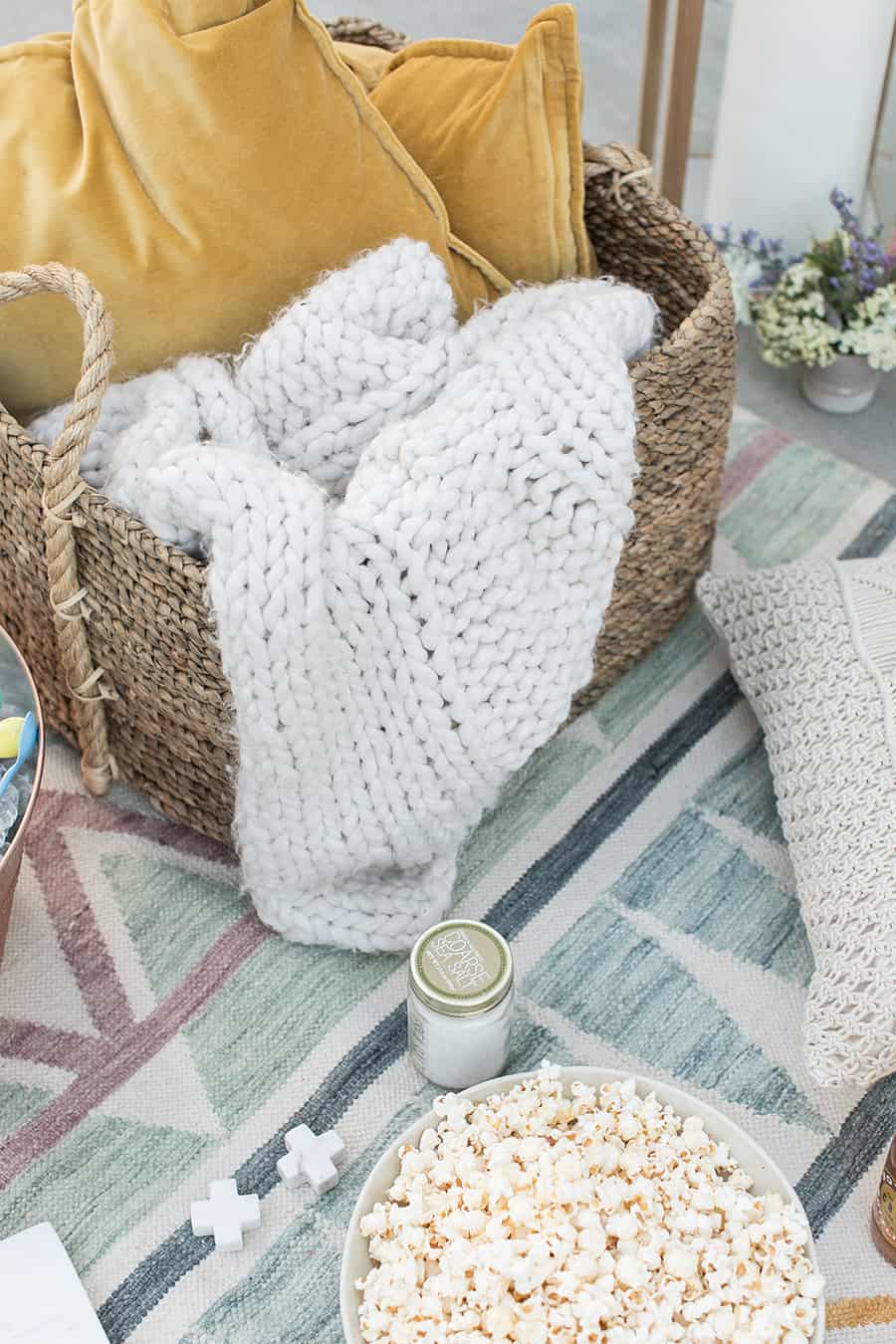 Basket with knitted blanket, bowl of popcorn on a modern blue rug. 