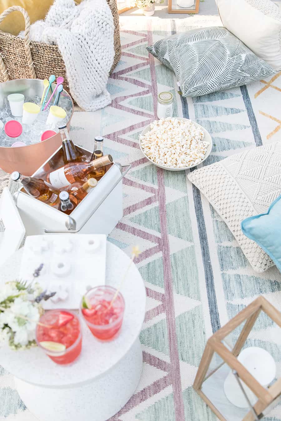 Outdoor movie night with pillows and popcorn, table with cocktails and rose in coolers. 