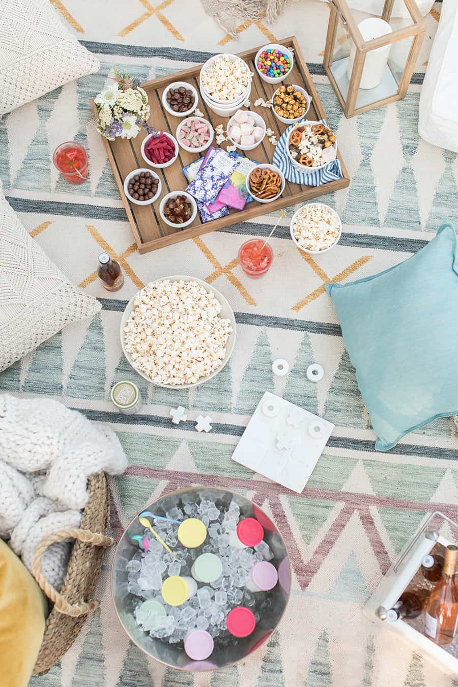 overhead picture of outdoor movie night with popcorn, pillows, games, tray of candy.