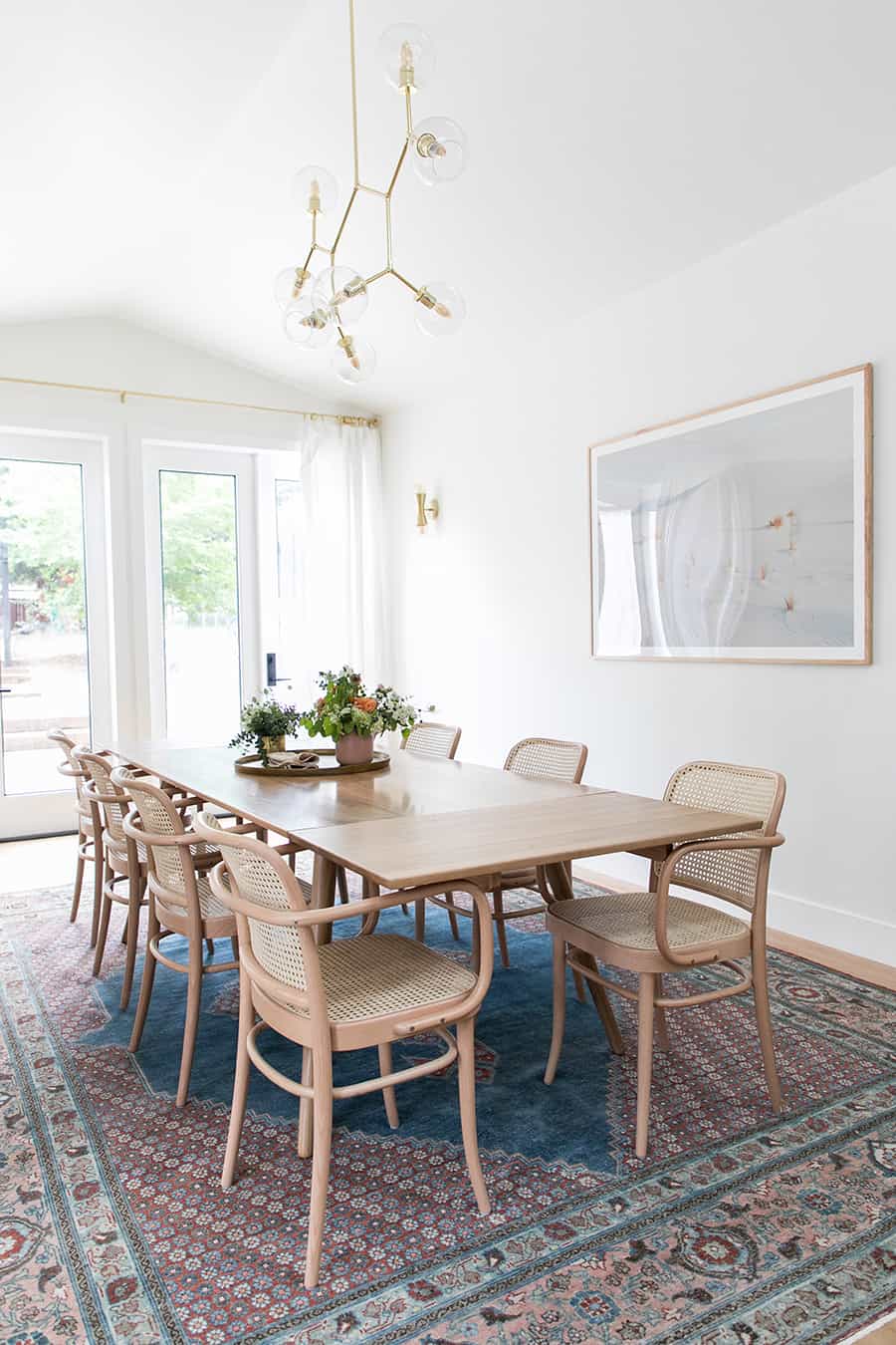 Dining room with blue rug, long table and white curtains