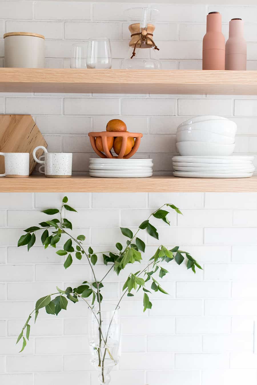 Long wooden open shelving with white plates and white tile.