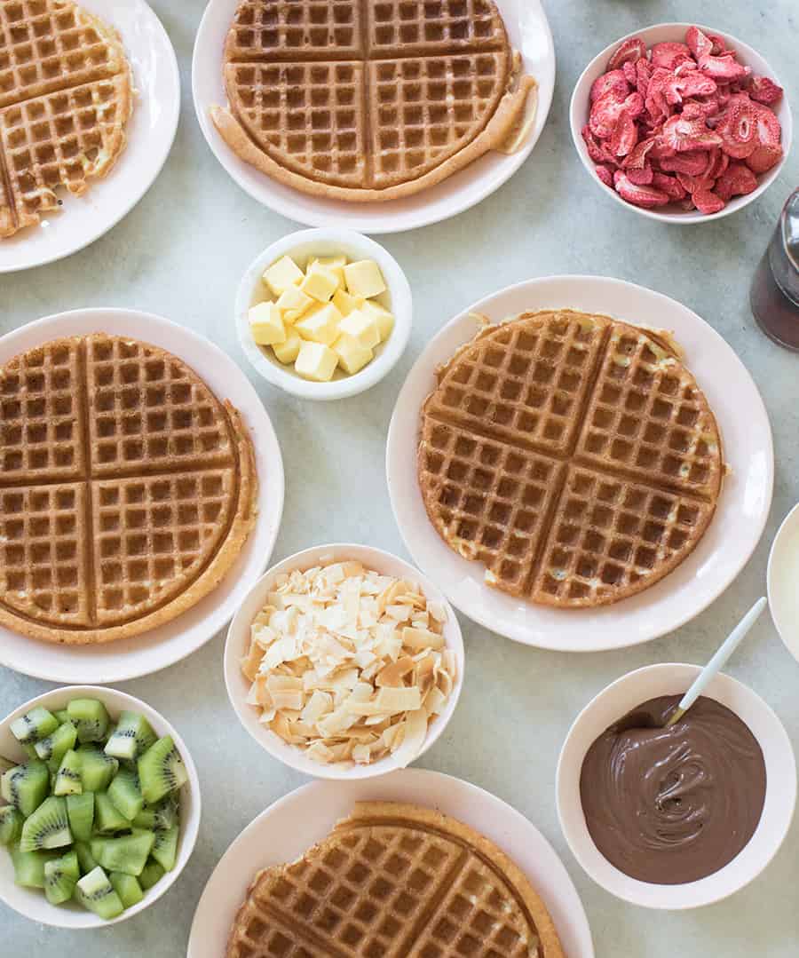 homemade waffle recipe with butter, coconut, berries on a table.