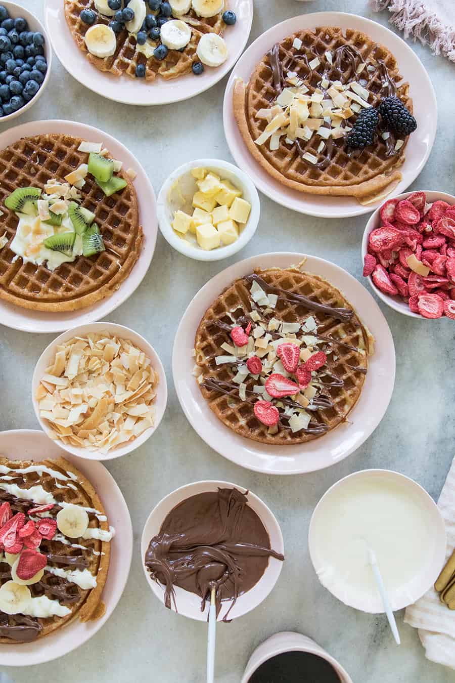 Overnight waffles on pink plates with fruit and chocolate toppings.