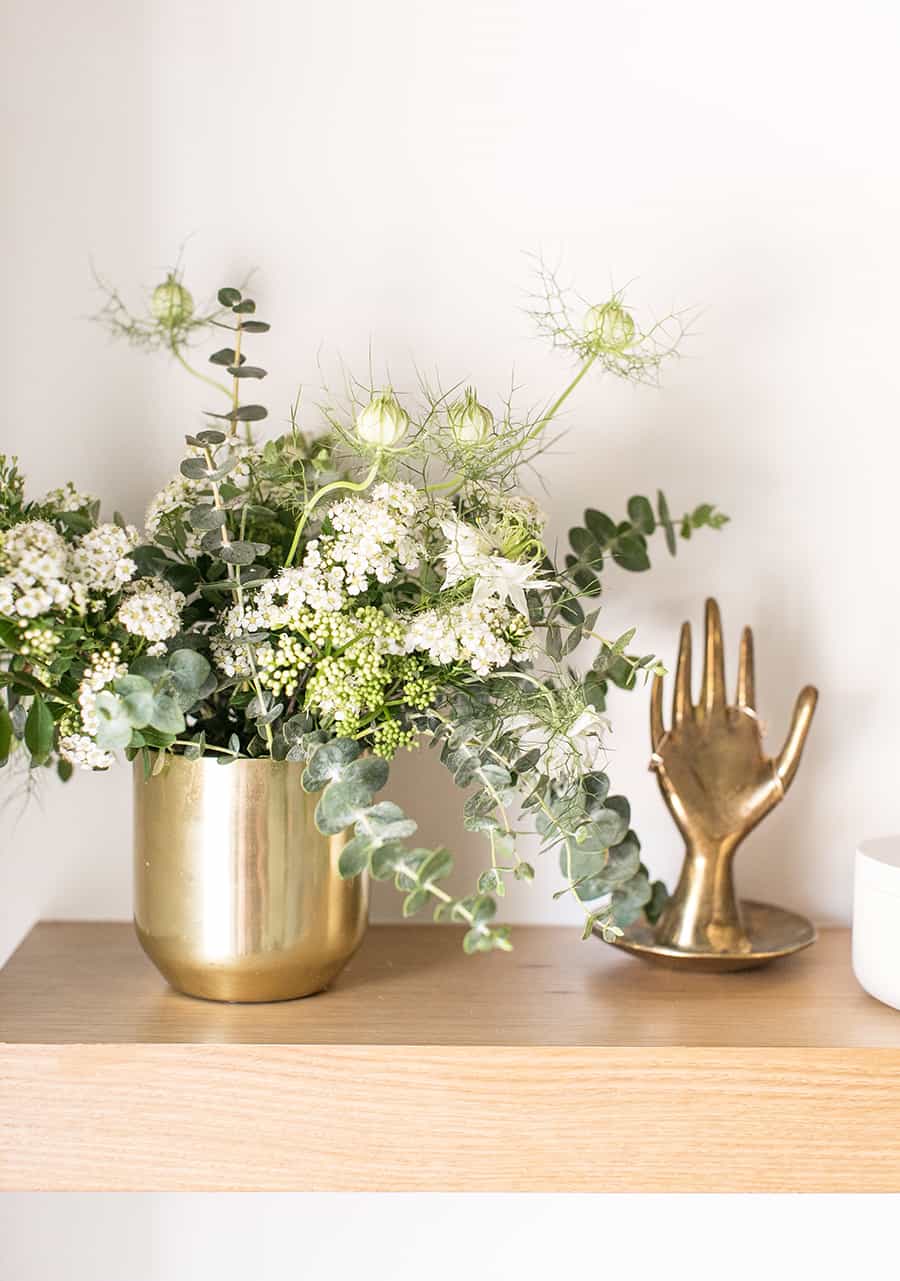 Gold vase with flowers and a gold hand with rings.