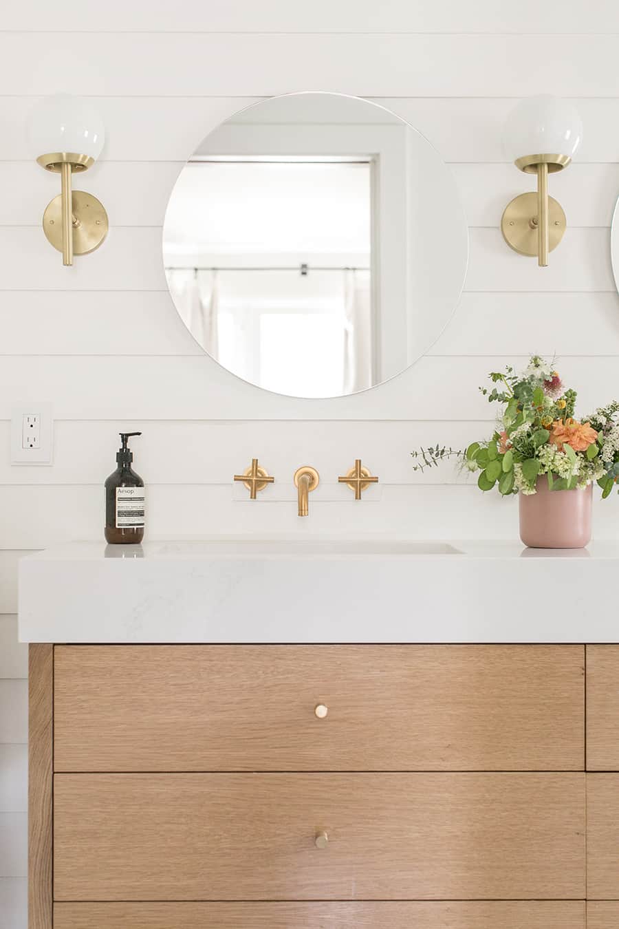 Charming bathroom vanity with thick counter top and three drawers, round mirror and flowers. 