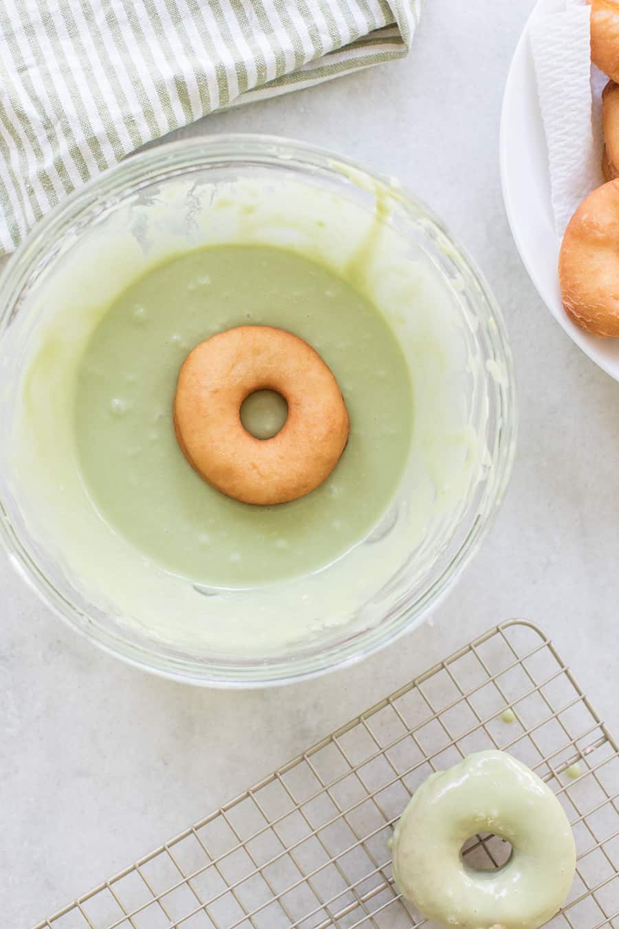 homemade donut being dipped into a white chocolate matcha glaze