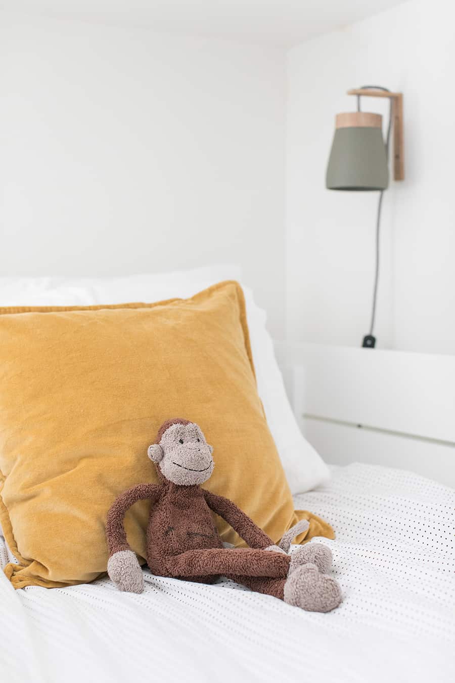 Kids bedroom with velvet yellow pillows and a stuffed monkey.