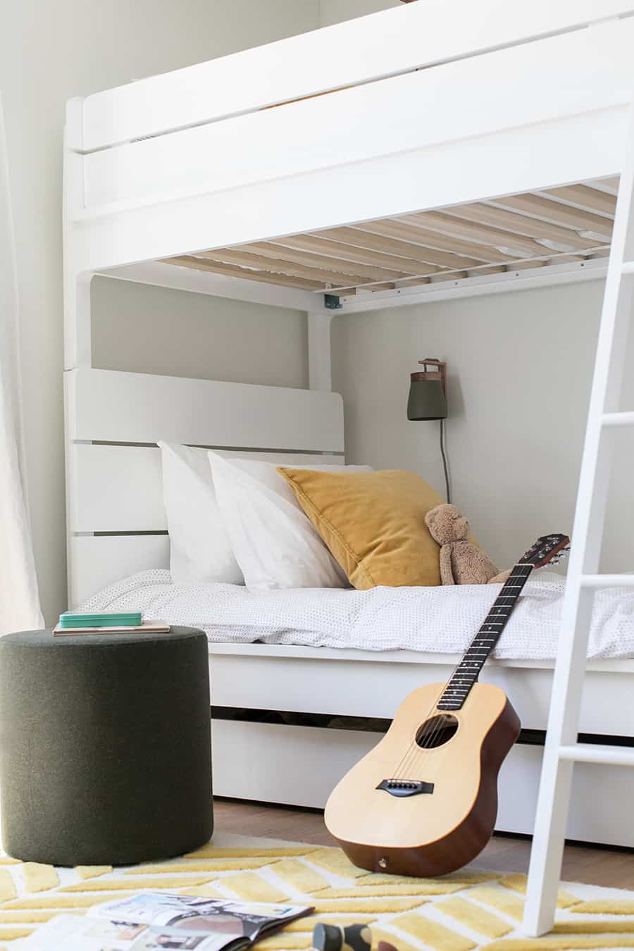 White bunkbeds in a boys room with yellow pillow, white bedding and a guitar.