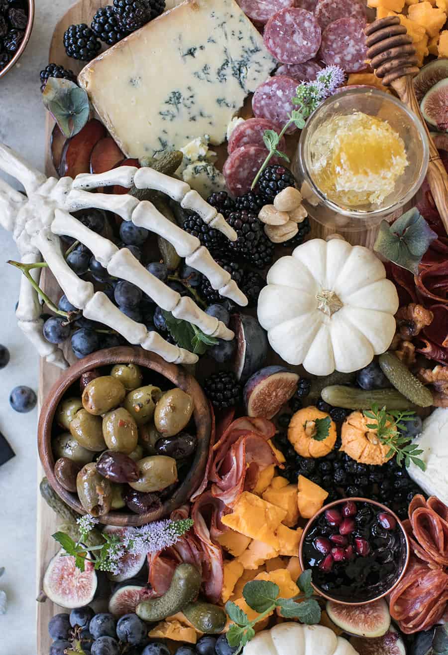 Skeleton hand on a Halloween Meat and Cheese Board with pumpkins, berries, pickles, olives, cheese and meat.