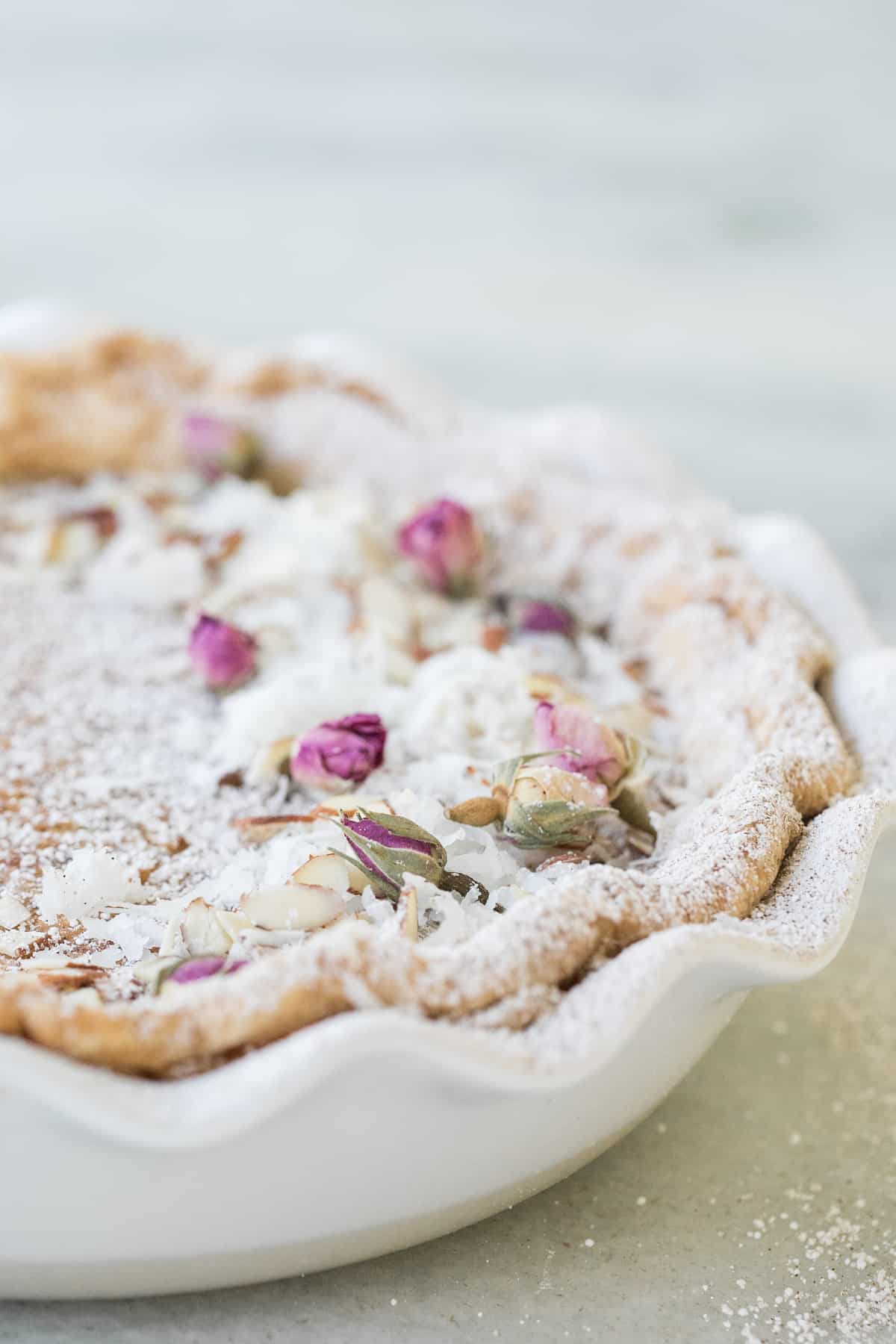 egg custard pie in a white pie dish with edible flowers and powdered sugar dusted over the top