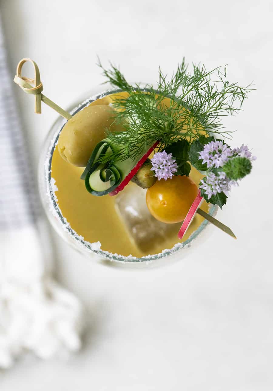 Overhead of a tomatillo bloody Mary with cucumber, olives and tomatoes.