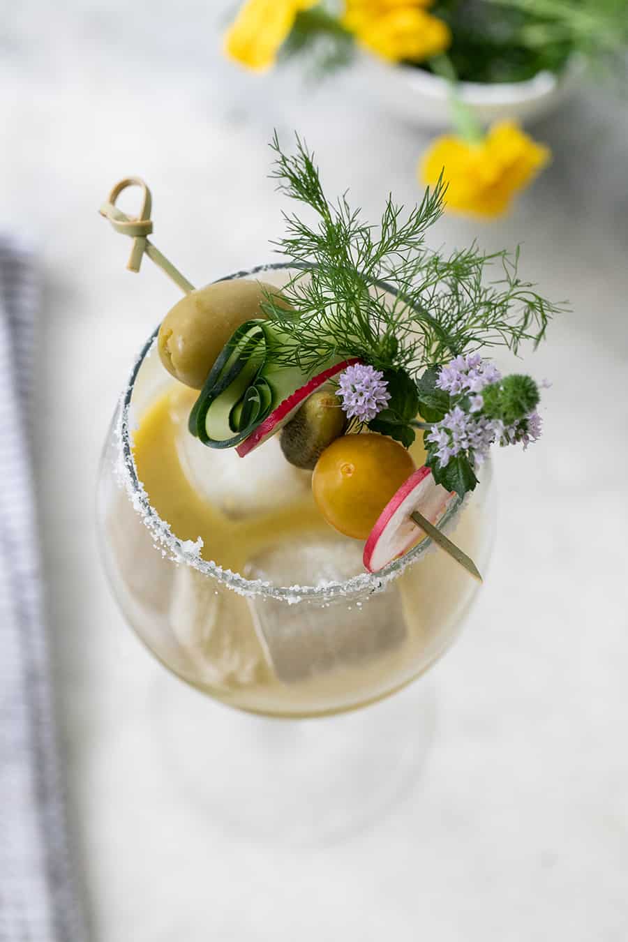 Tomatillo Bloody Mary in a glass with olives, flours, pickle 