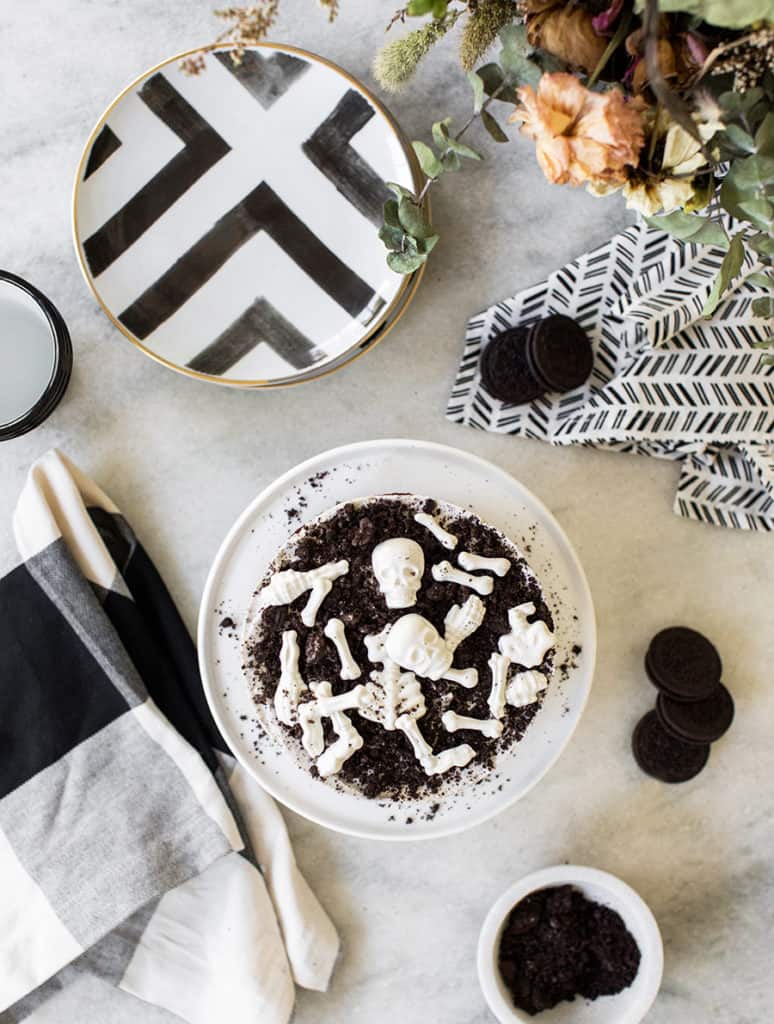 overhead of an Oreo cake with candy skull bones and black and white plates with black and white napkins on a marble table.