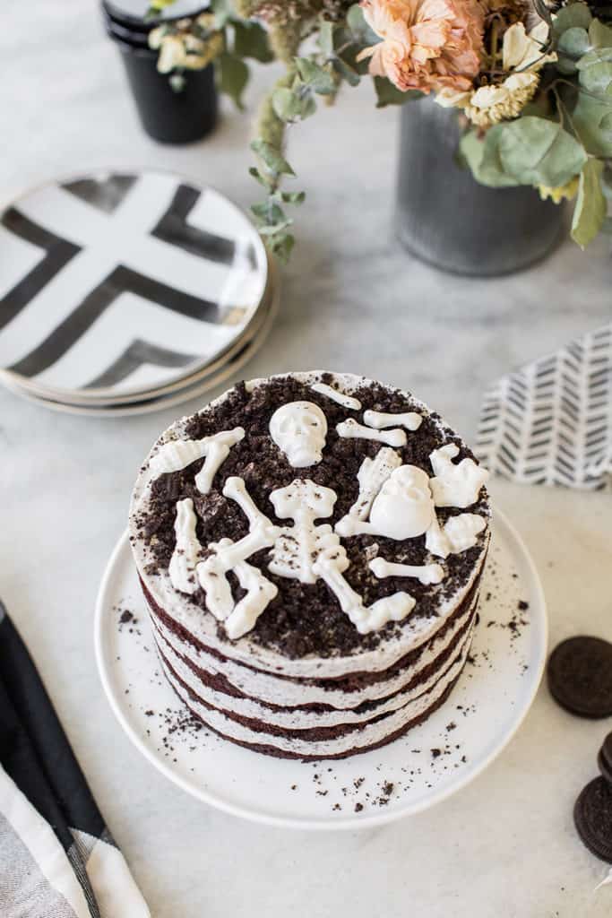 overhead of Oreo cake with white chocolate candy bones on marble table with cake stand.