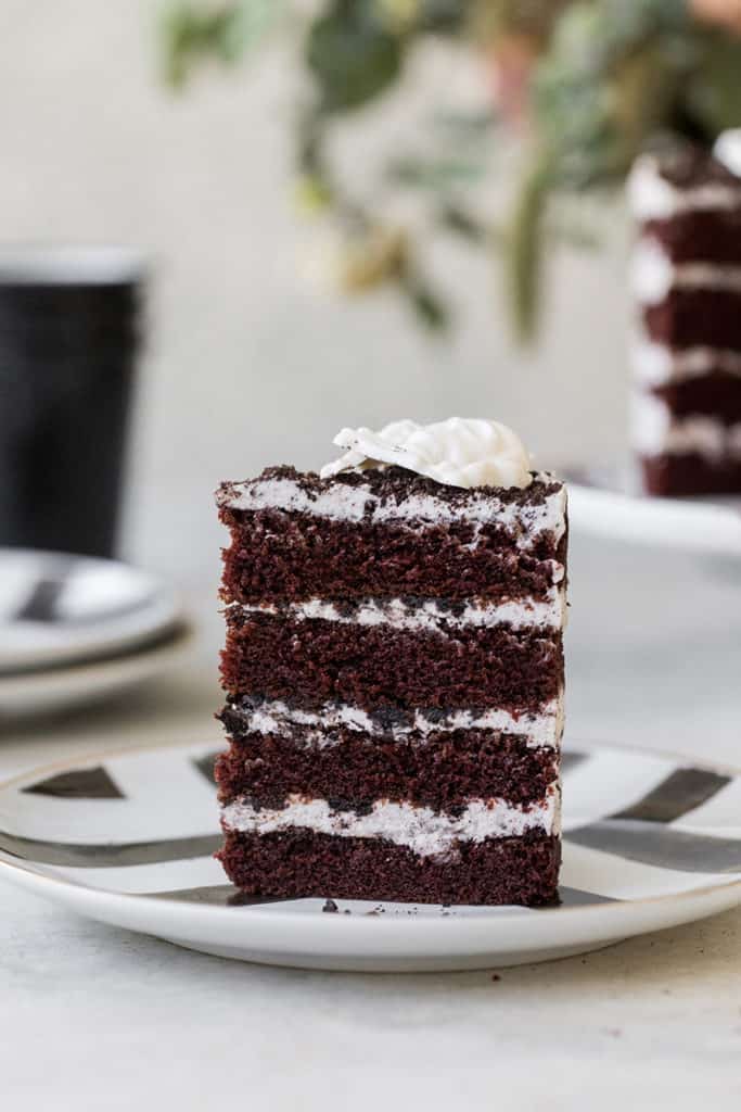 Slice of chocolate cake with layered vanilla frosting standing up on a plate