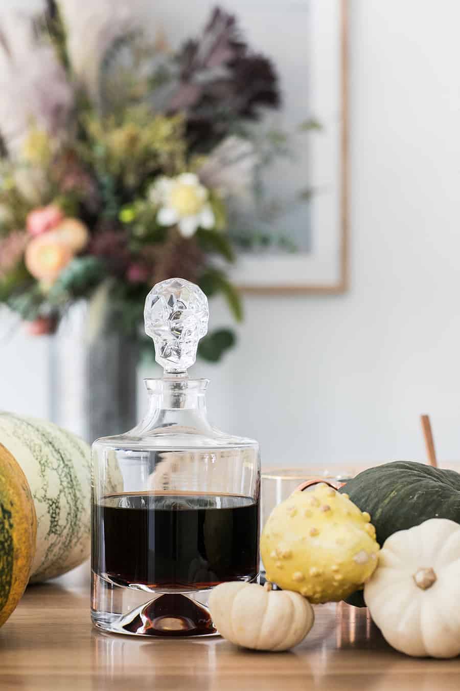 Skull decanter with dark rum and pumpkins on a table.