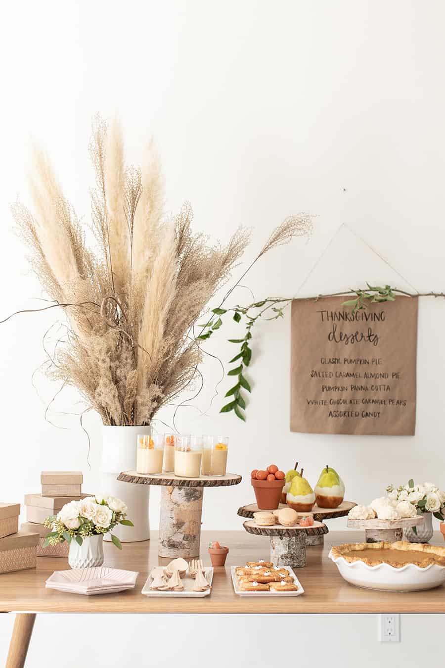 Thanksgiving dessert table with birchwood cake stands and flowers in a white vase.