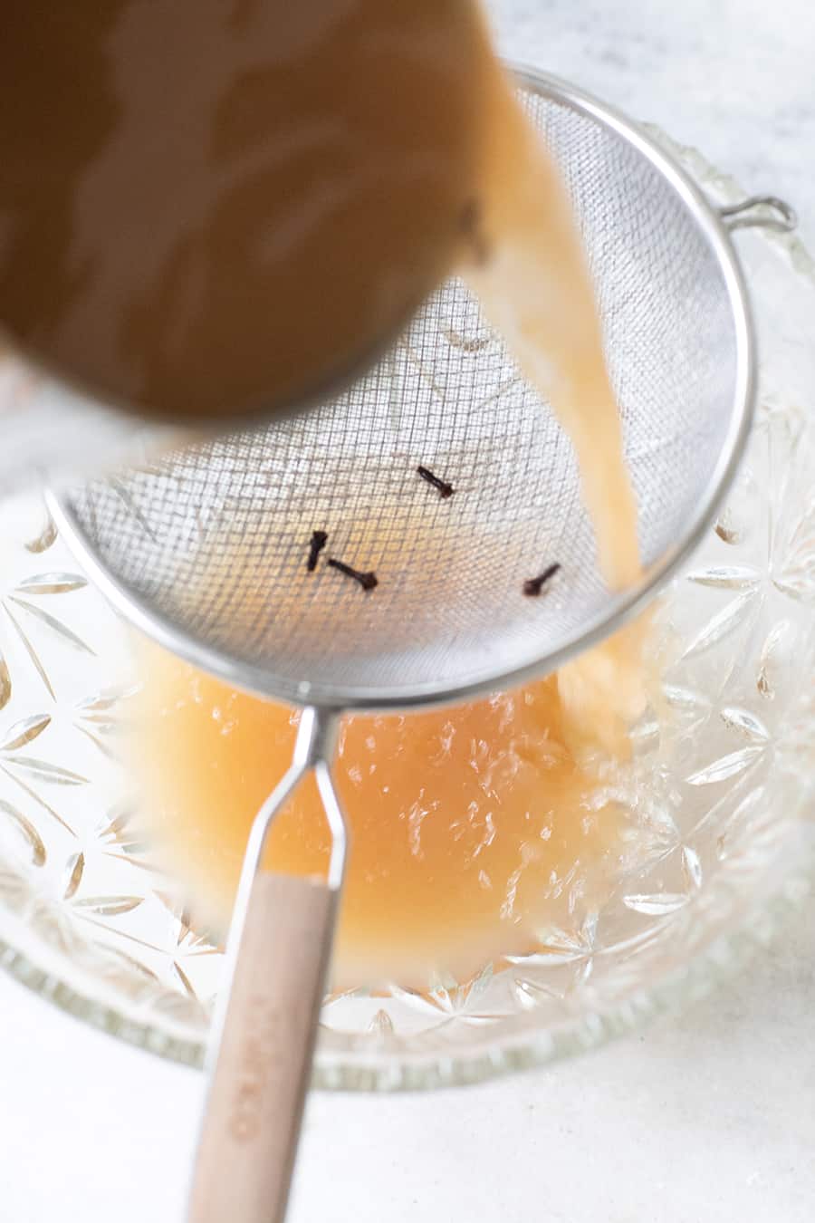 Pouring a cider into a bowl through a sieve to make a holiday punch.