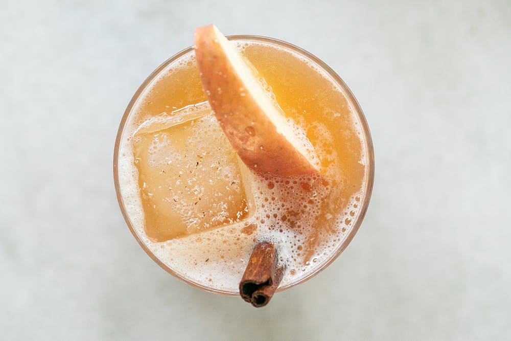 Apple cider bourbon cocktail with cinnamon and and sliced apple.