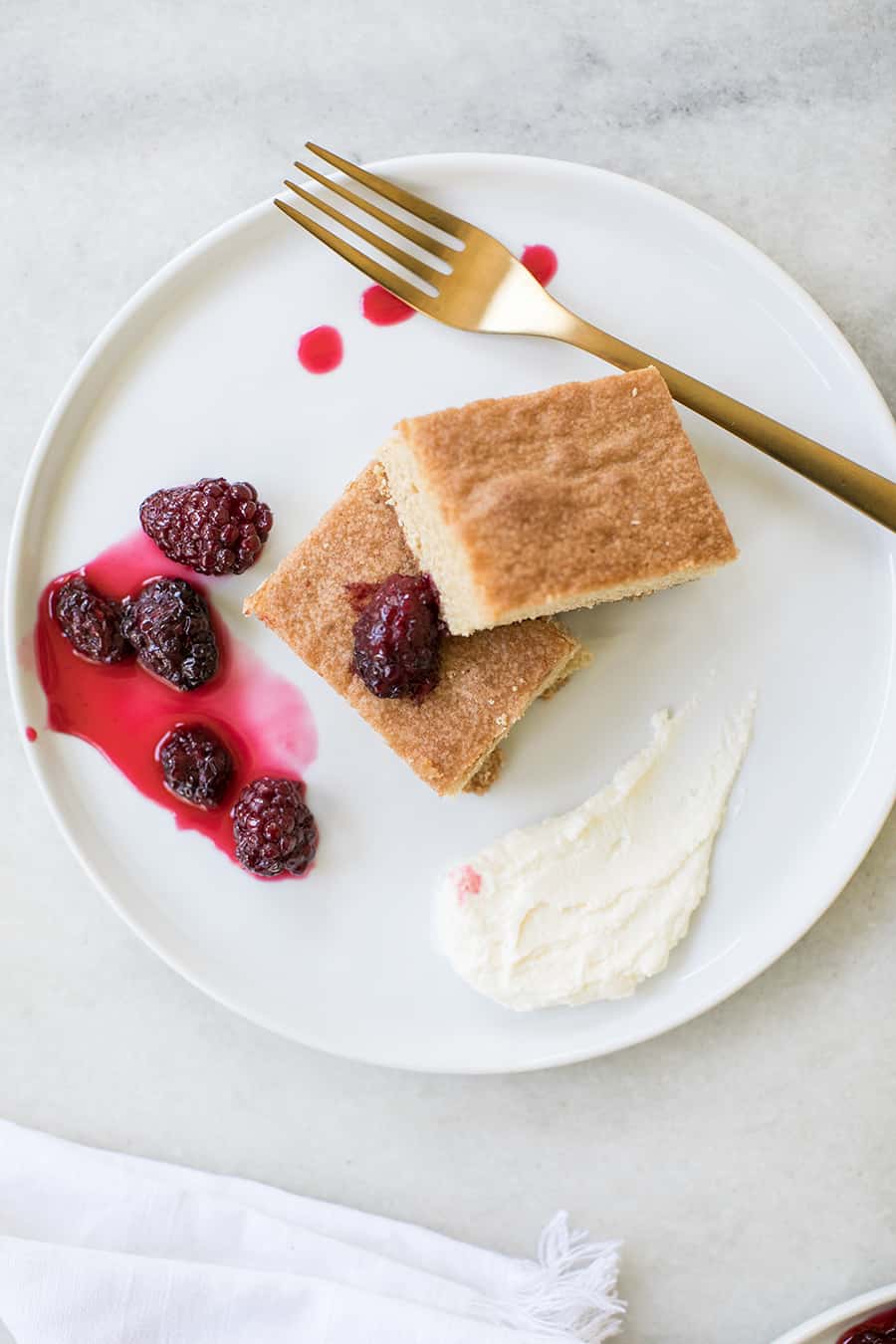 Brown sugar cake on a white plate with blackberries.