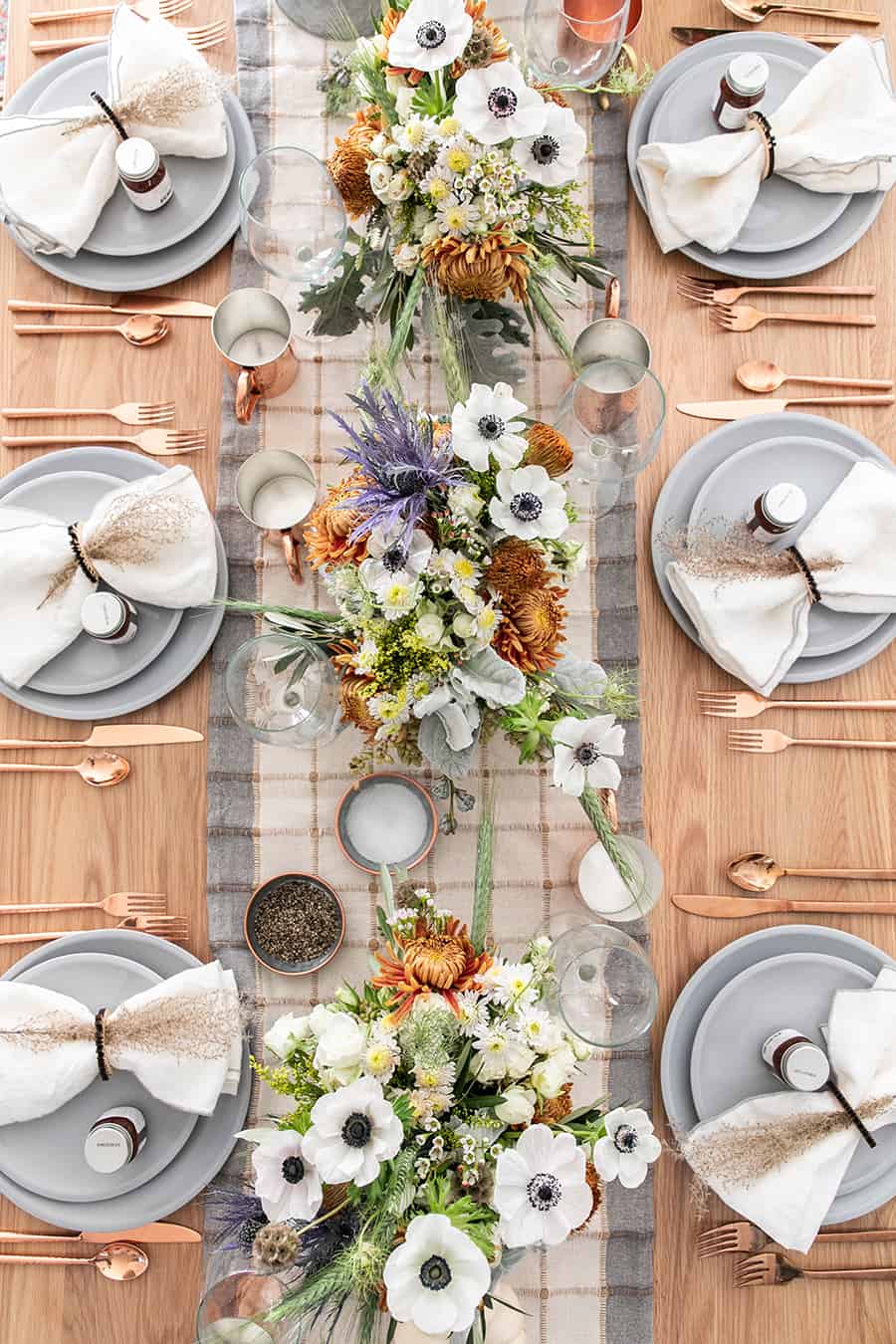 A rustic and modern tablescape with flowers, table runner, wine glasses, copper silverware. 