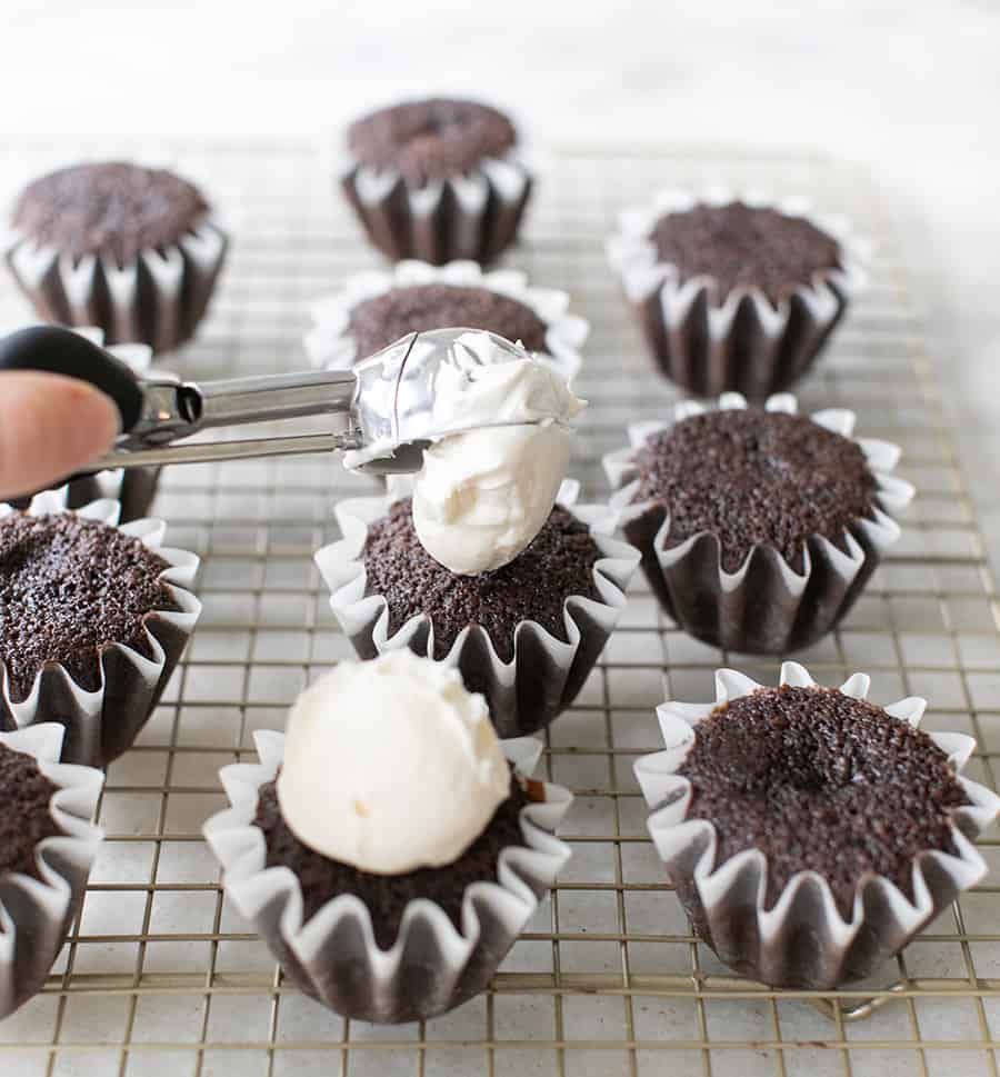 frosting being scooped onto a chocolate cupcake