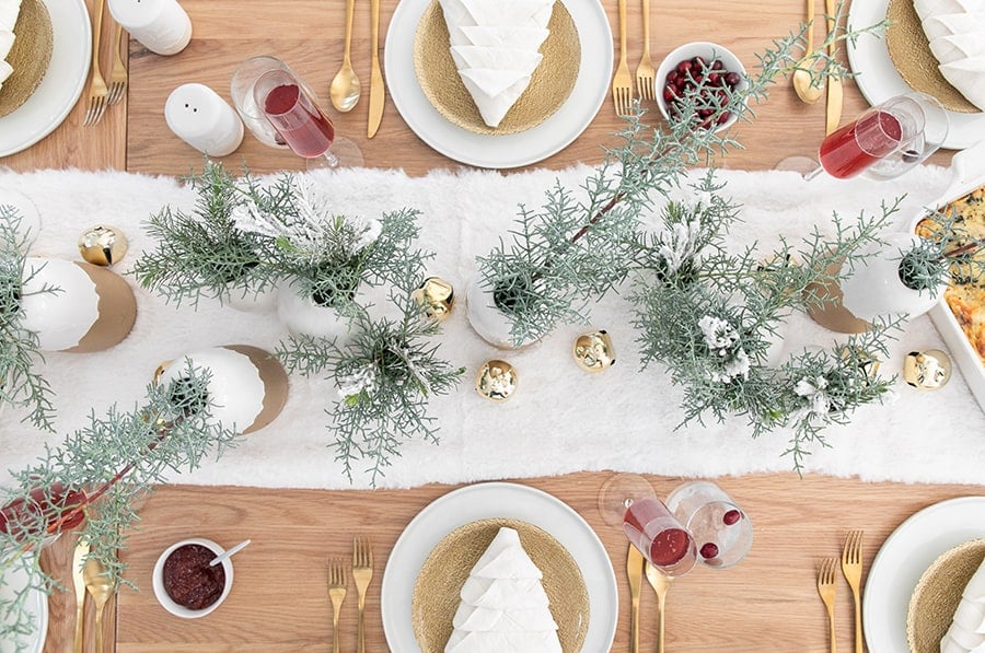 Christmas table setting with greens and a furry white table runner. 