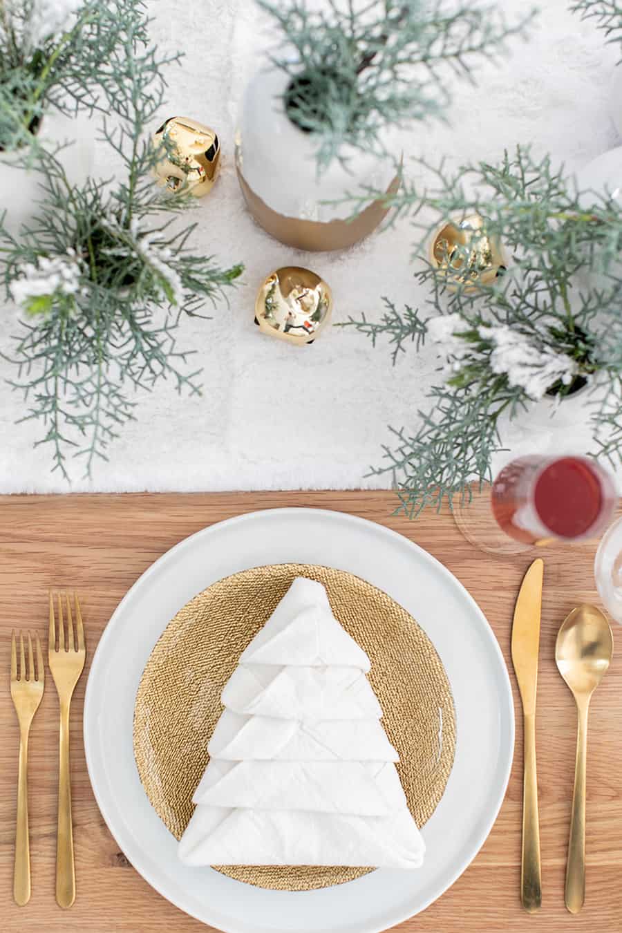 White napkin folded like a Christmas tree on a gold plate with gold utensils. 