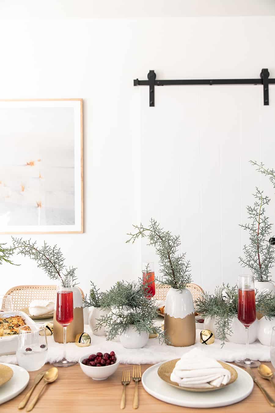 Table setting for Christmas brunch with white and gold vases and Christmas greens.