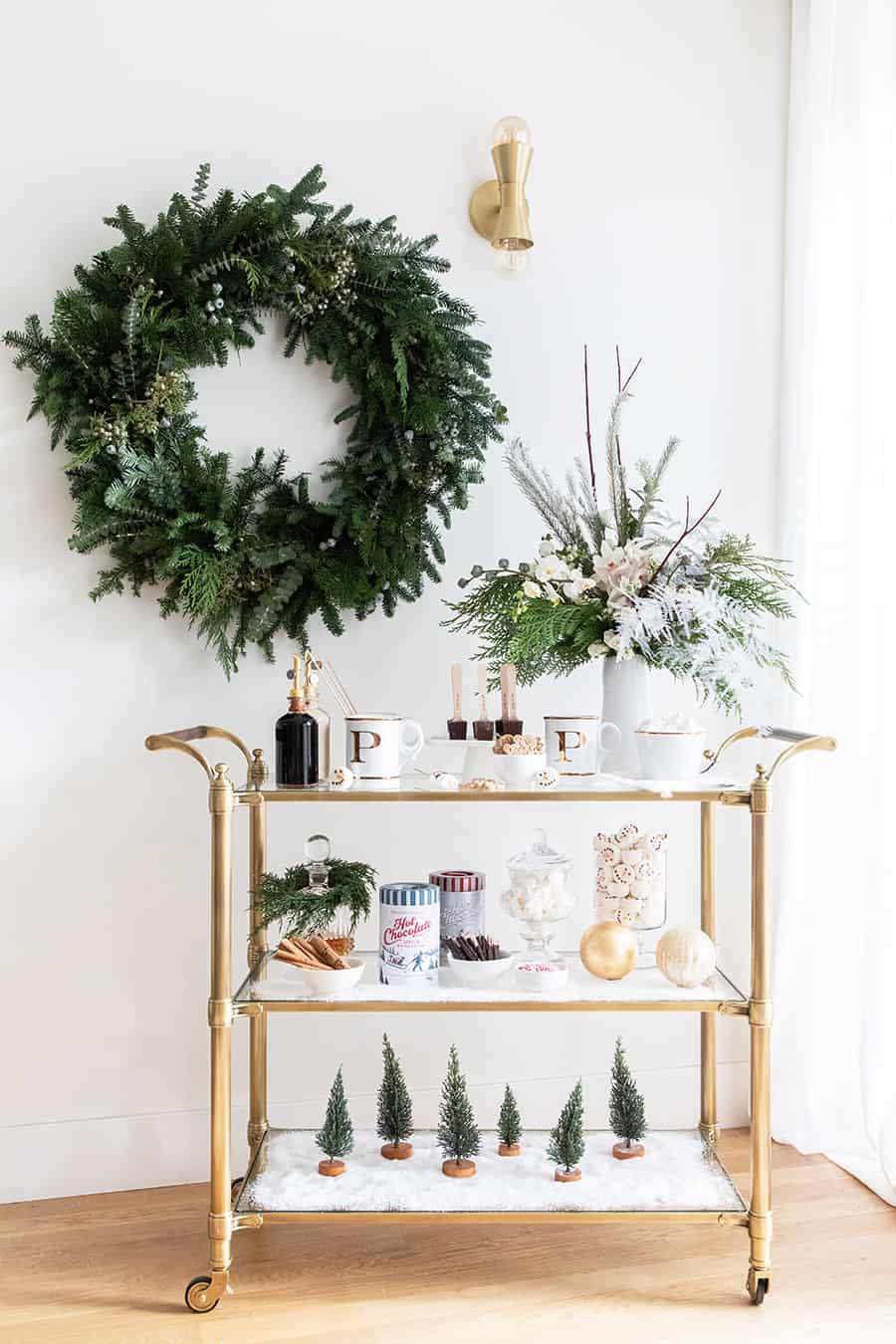 Hot chocolate bar on a gold bar cart with a wreath on the wall.